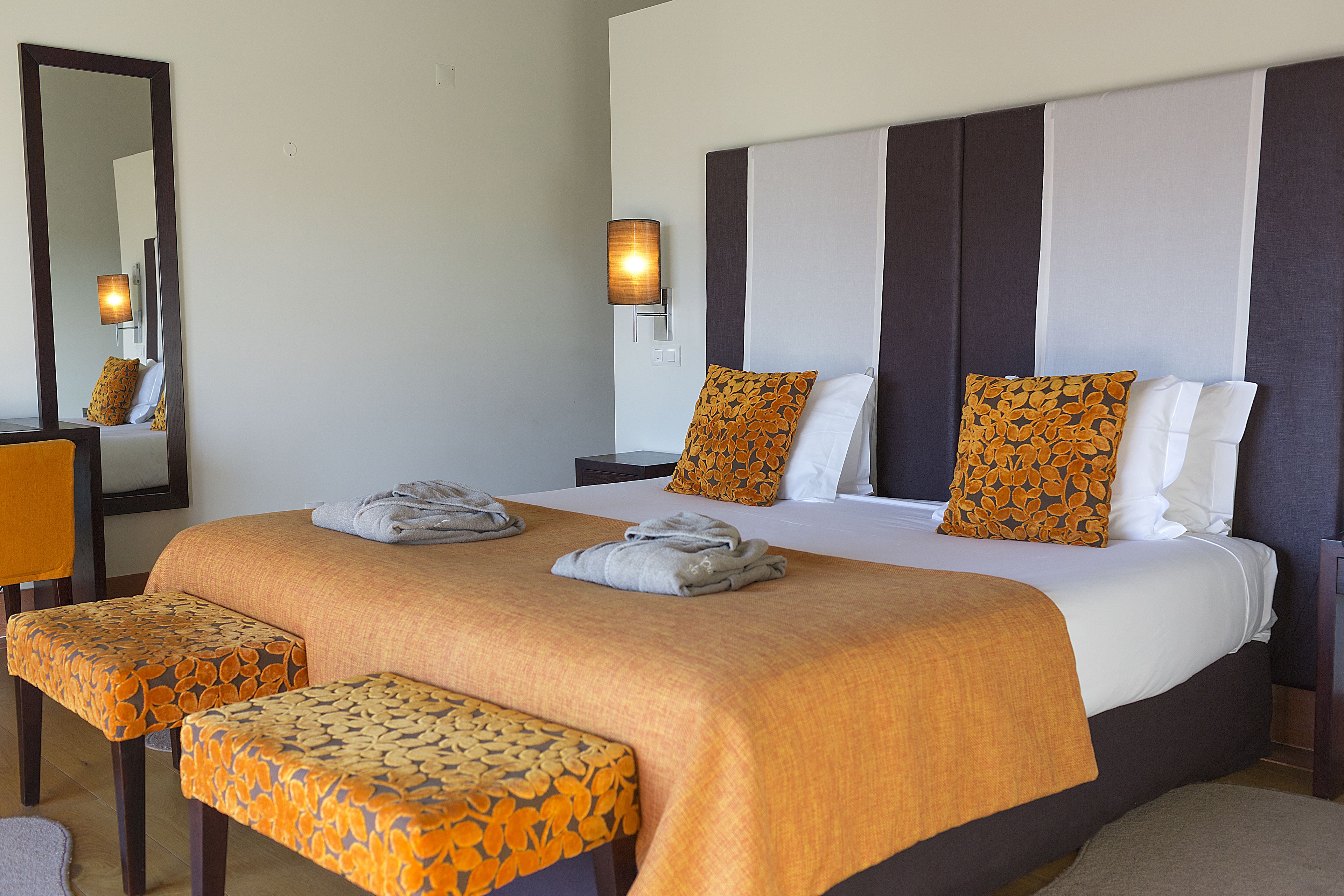 A hotel room with a large bed, two bedside tables, a mirror, and a wall-mounted lamp.