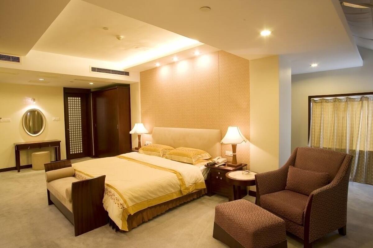 Una habitación de hotel con una cama grande, lámparas de noche, una silla, una mesita y un espejo.