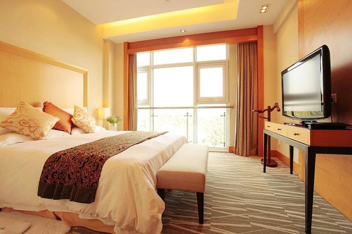 Habitación de hotel con una cama grande, un televisor sobre un mueble de madera y una ventana con cortinas.