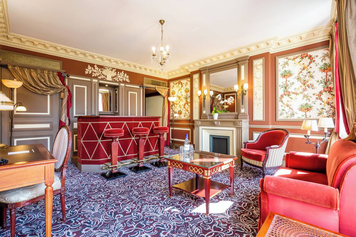 A luxurious room with a patterned carpet, a red sofa, a glass coffee table, and a fireplace.