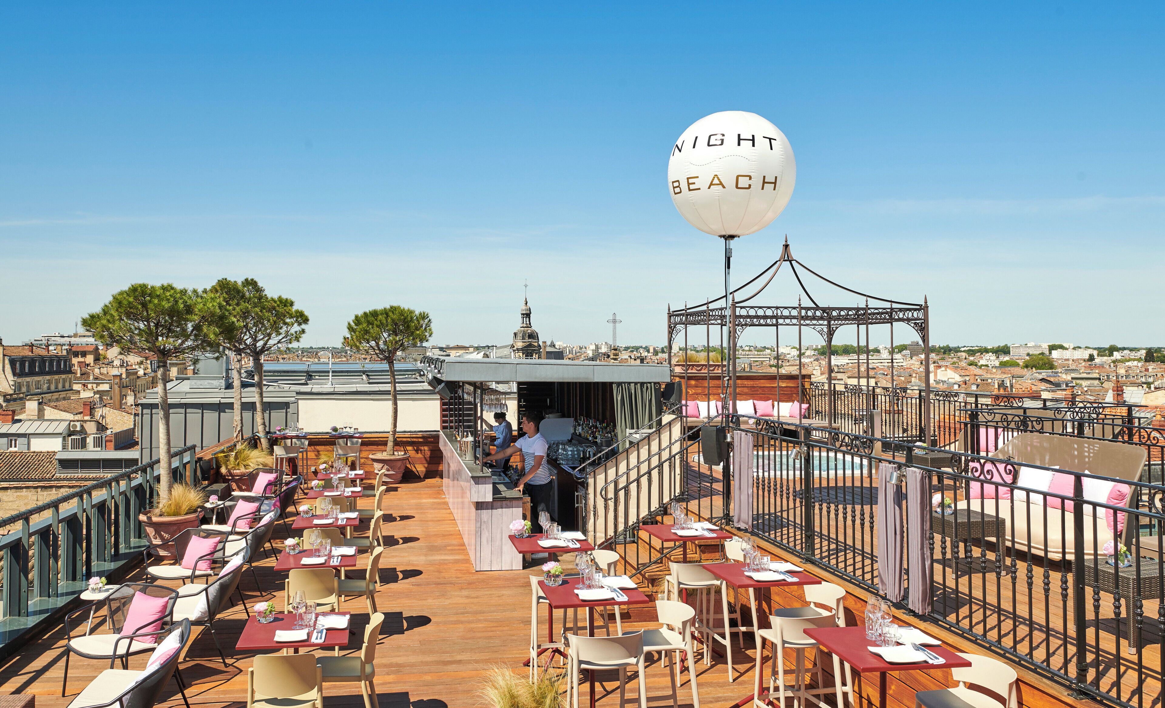 Un espacio exterior con mesas y sillas, un bar y vistas a la ciudad.
