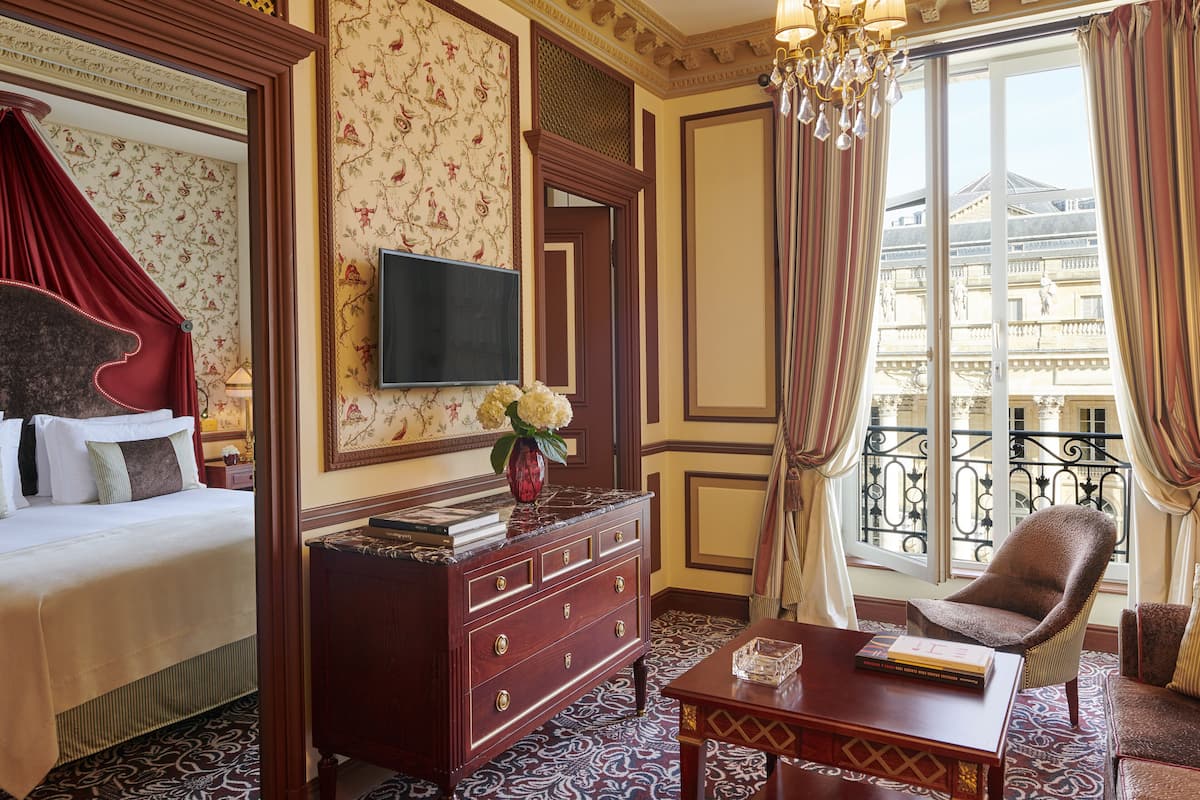 A hotel room with a bed, a dresser, a television, a chair, and a window with a view of a building.