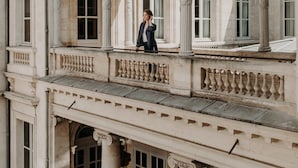 A classical building with a balcony, columns, and a person standing on it.