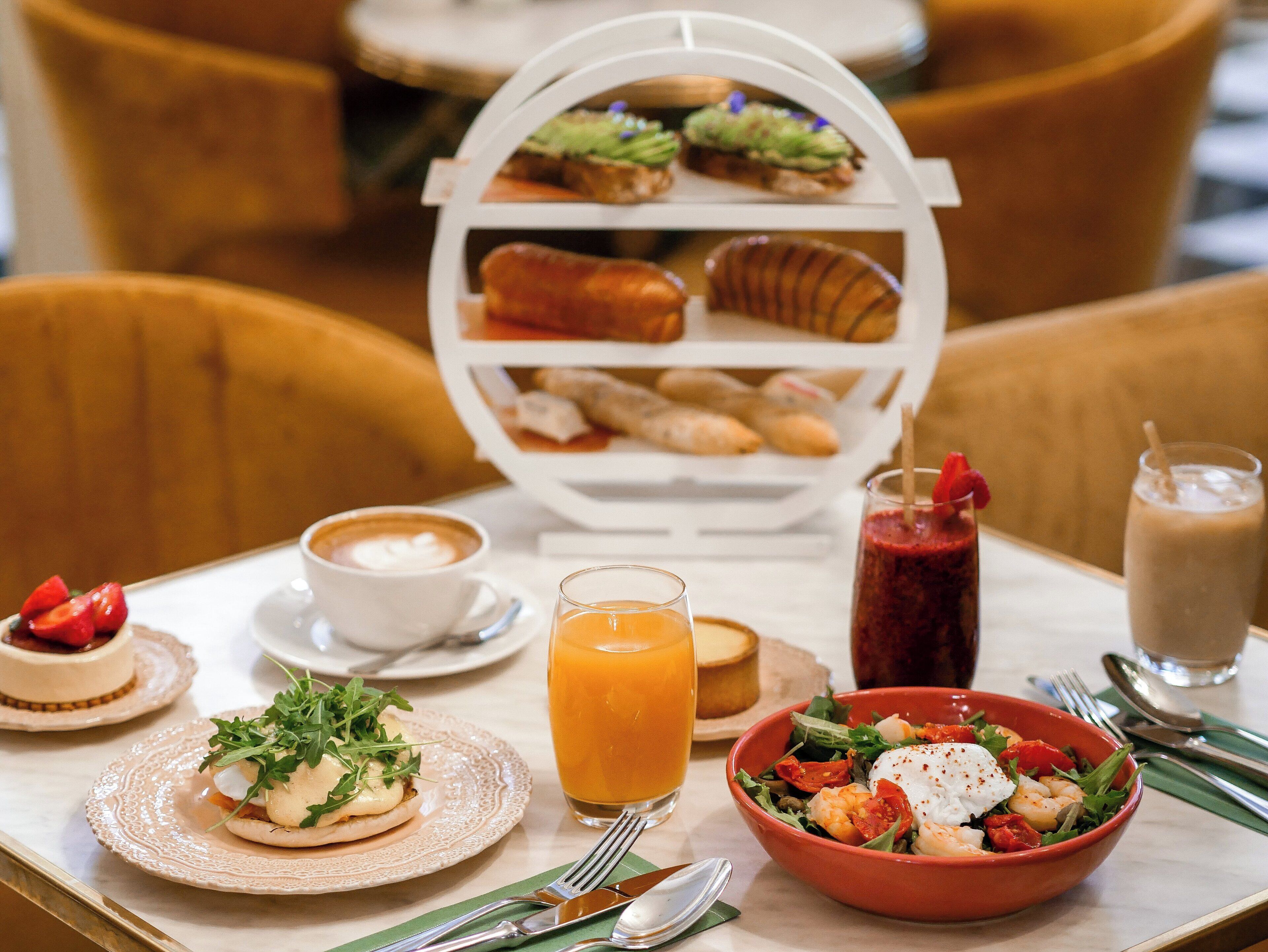 Une table dressée pour le petit-déjeuner, avec une variété d’aliments, notamment un bol de salade, une assiette d’œufs, une tasse de café et un verre de jus d’orange.