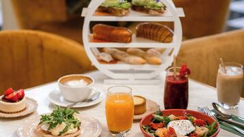 Une table dressée pour le petit-déjeuner, avec une variété d’aliments, notamment un bol de salade, une assiette d’œufs, une tasse de café et un verre de jus d’orange.
