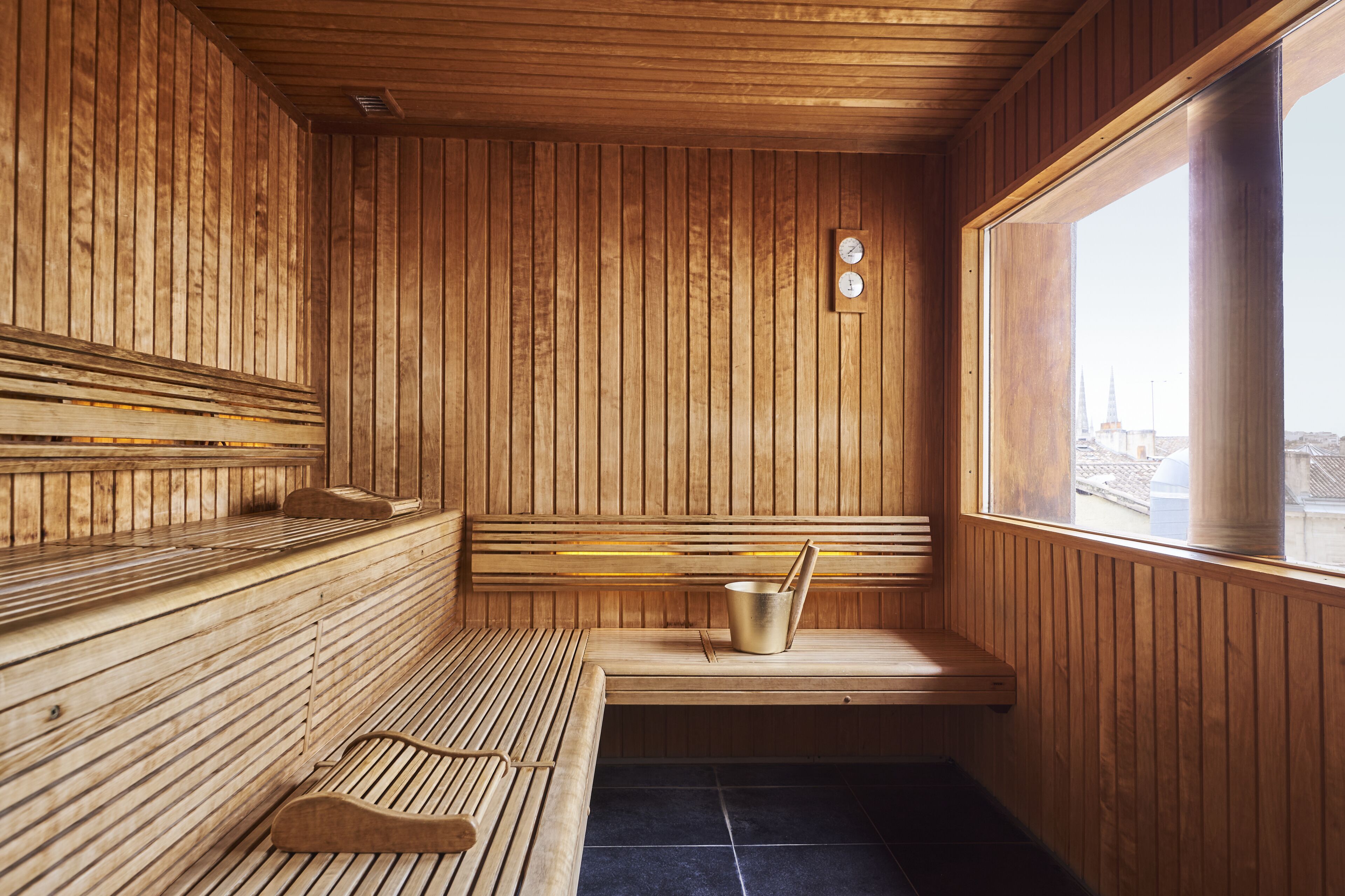 Sauna de fusta amb bancs, un cubell i un rellotge a la paret.