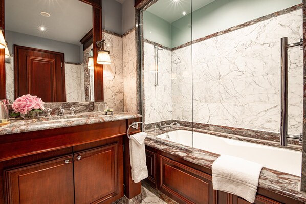 A luxurious bathroom with a marble sink, a large bathtub, and a glass-enclosed shower.
