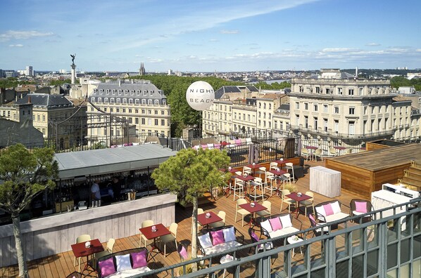 A rooftop bar with outdoor seating and a view of the cityscape.