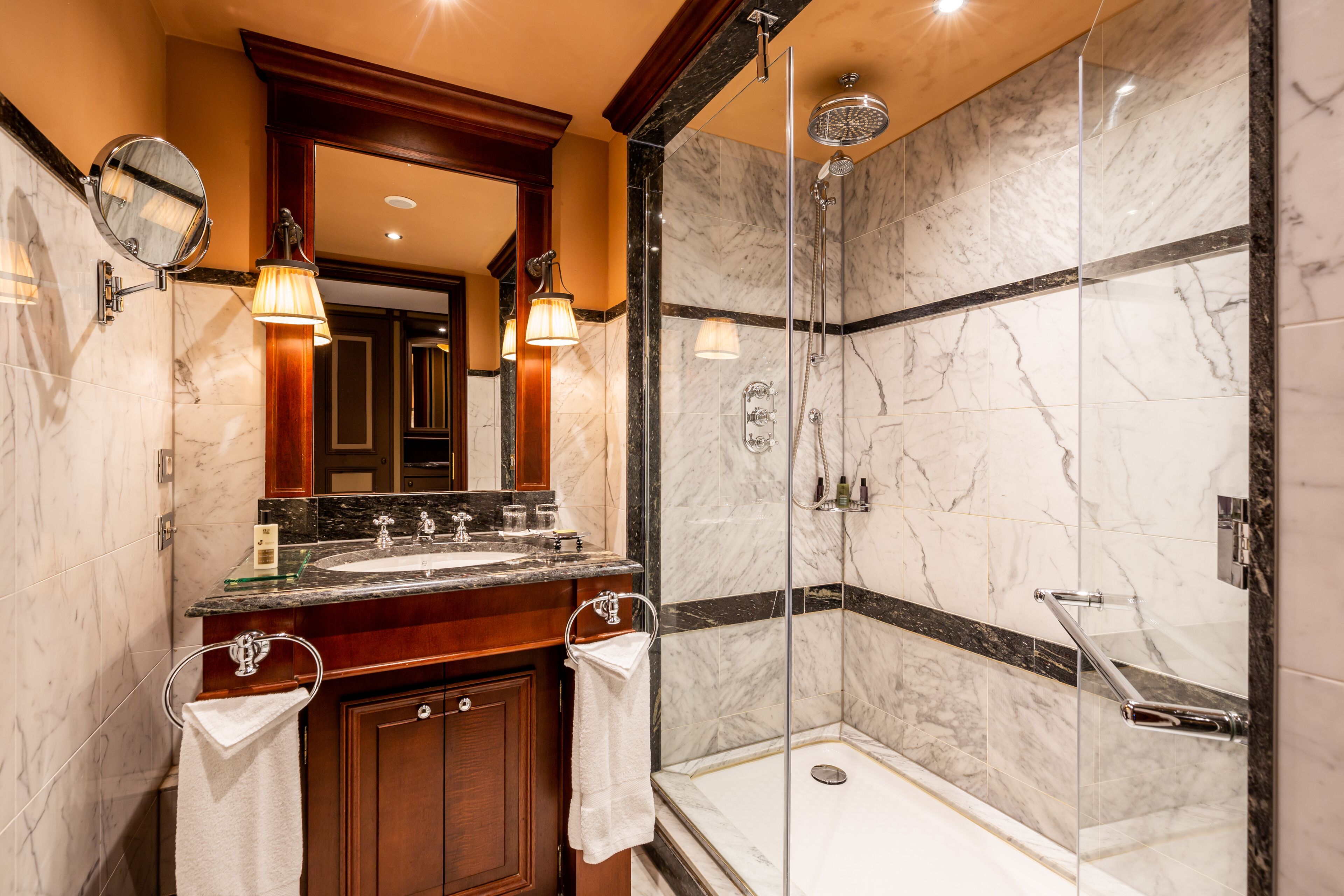 A modern bathroom with a glass-enclosed shower, a marble vanity, and dual sinks.