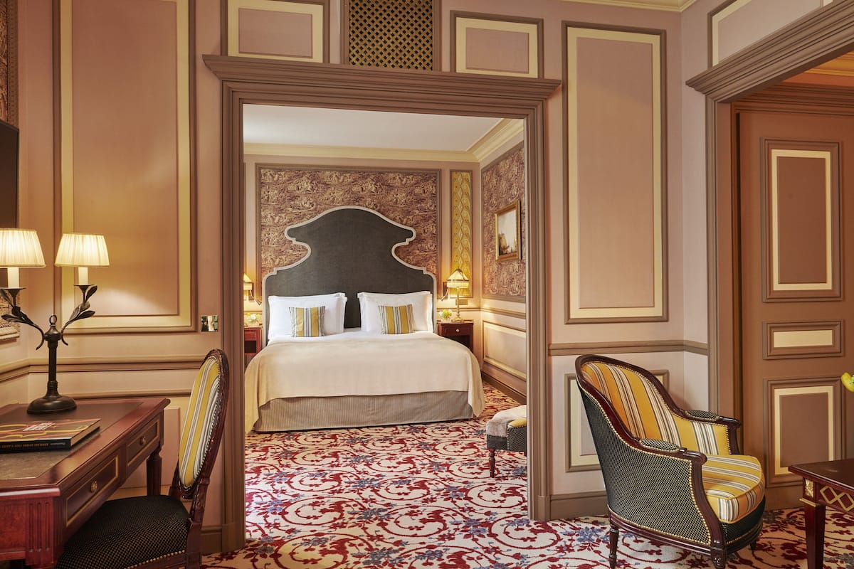 A hotel room with a large bed, a desk with a lamp, a chair, and a decorative wall.