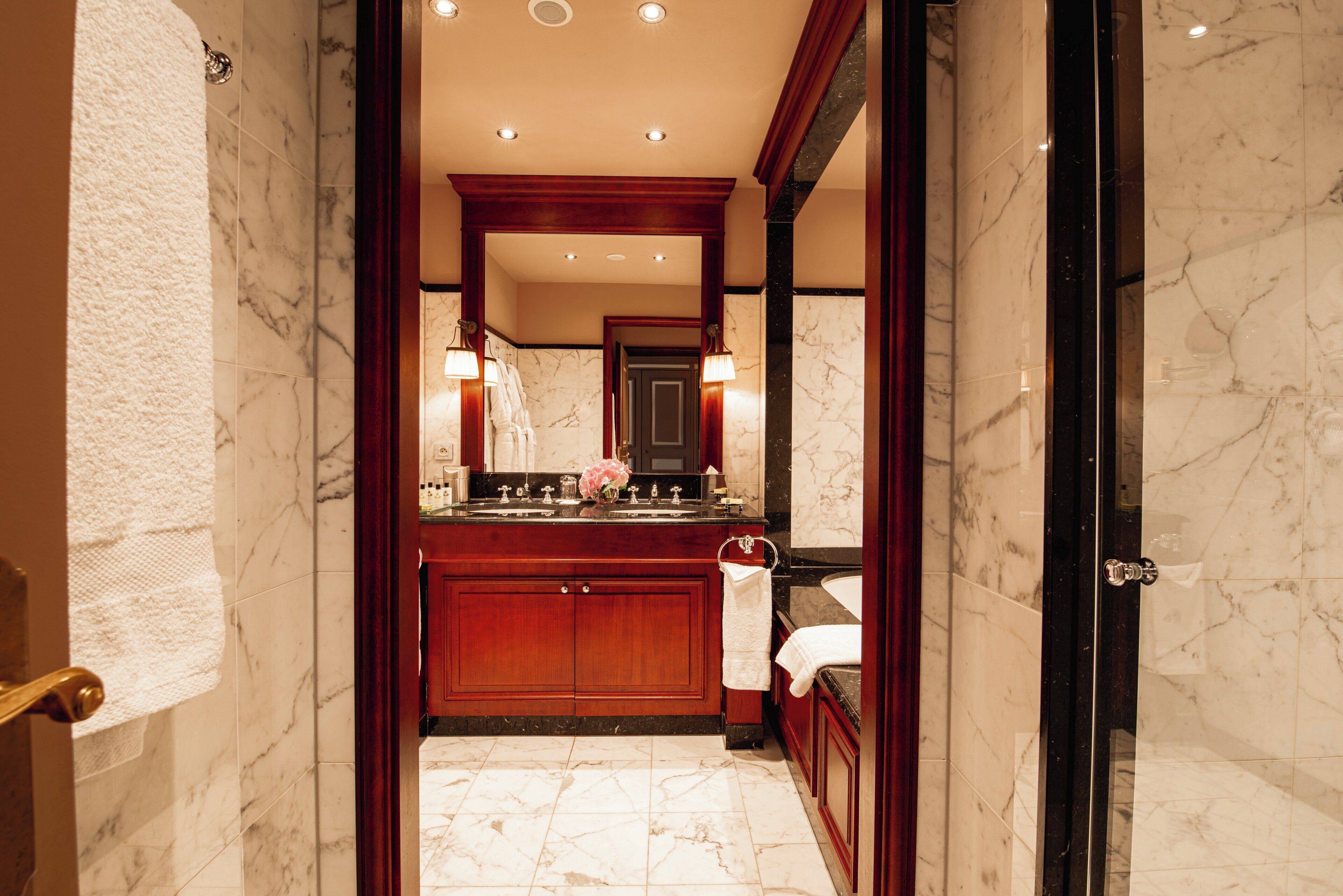 A hotel bathroom with marble flooring, a wooden vanity, a large mirror, and a bathtub.