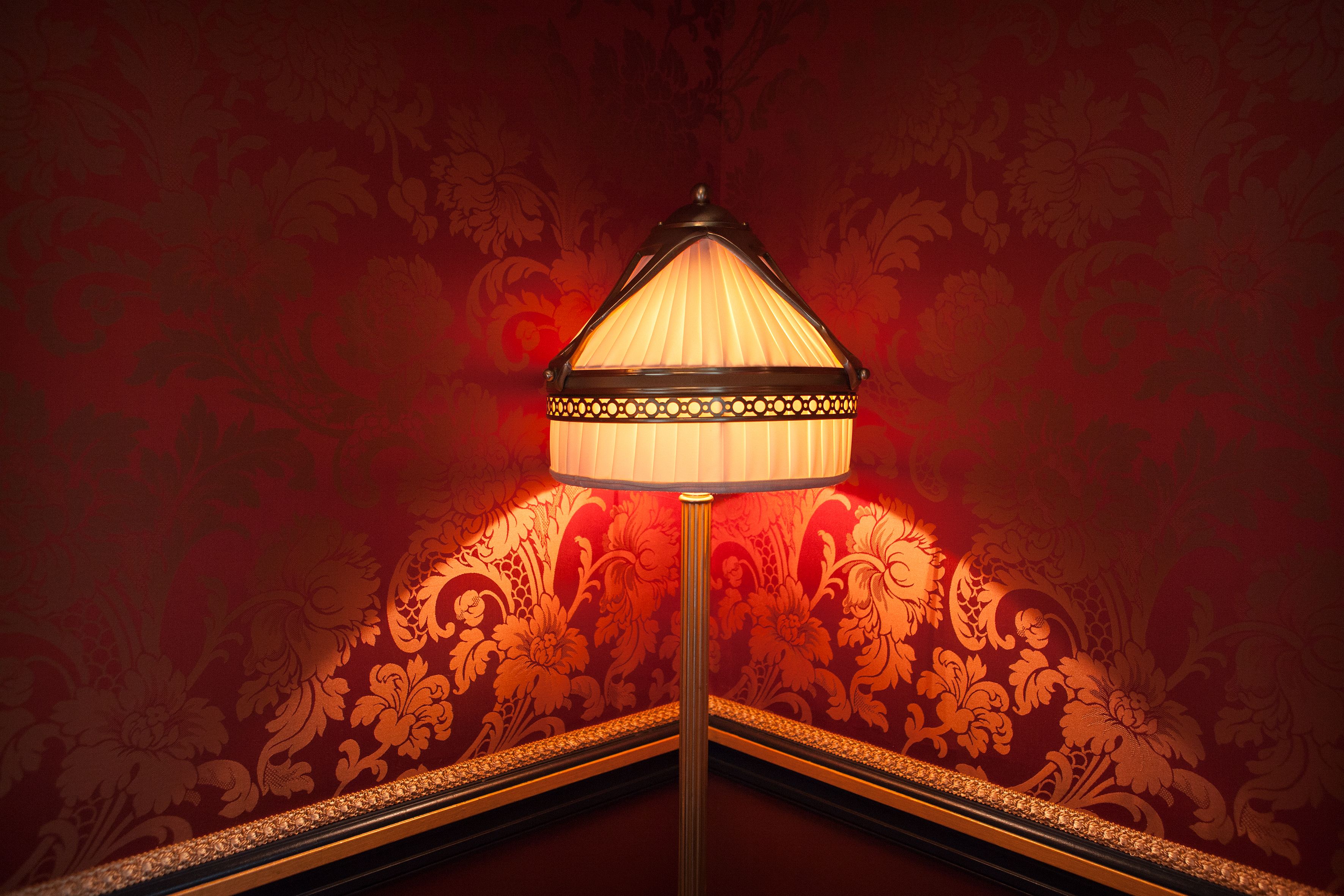A lamp with a decorative base and a patterned wall in the background.