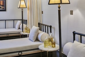 A hotel room with two beds, a small table with perfume bottles, and two standing lamps.
