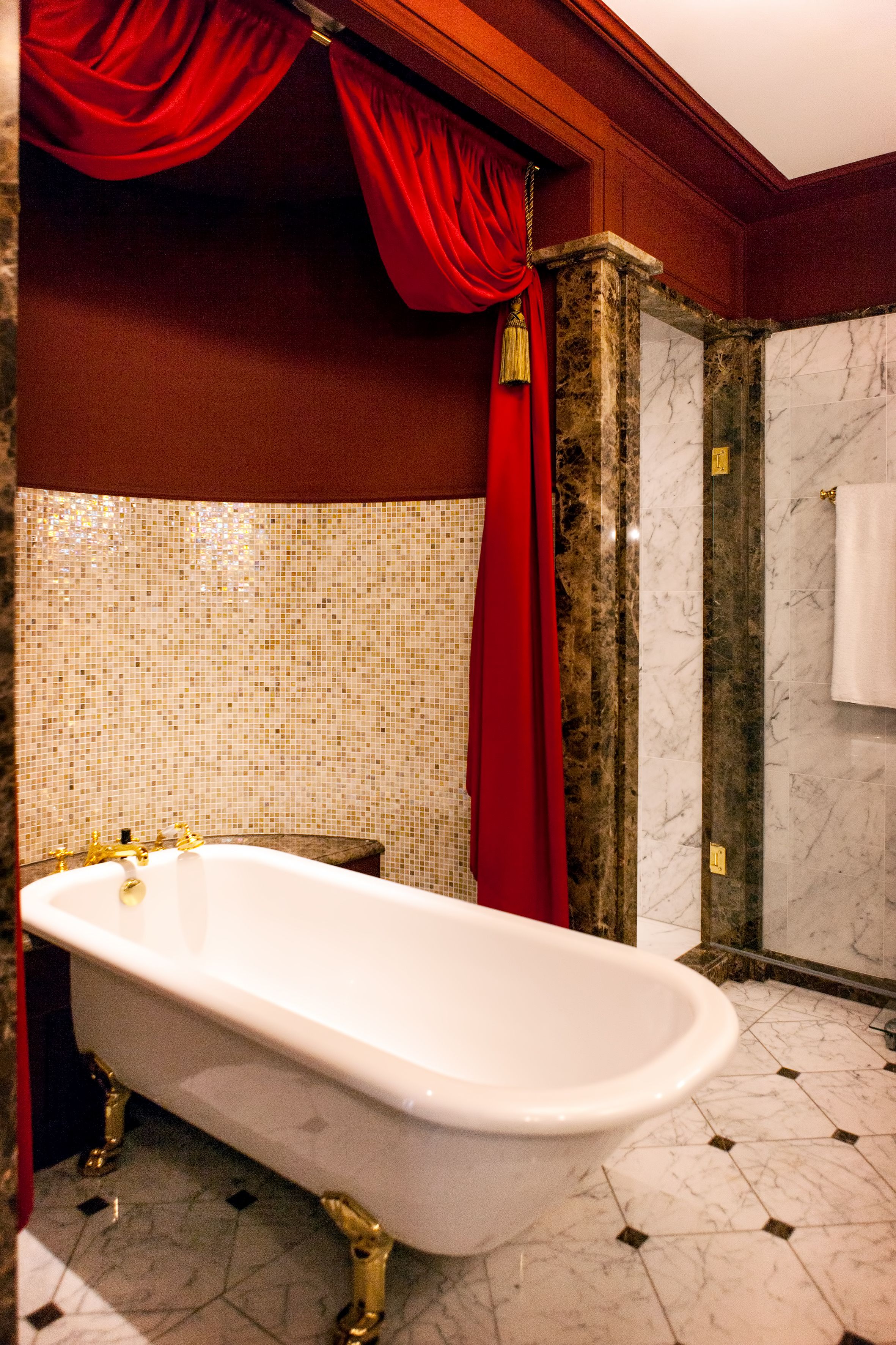 A bathroom with a freestanding bathtub, a tiled mosaic wall, and a marble column.