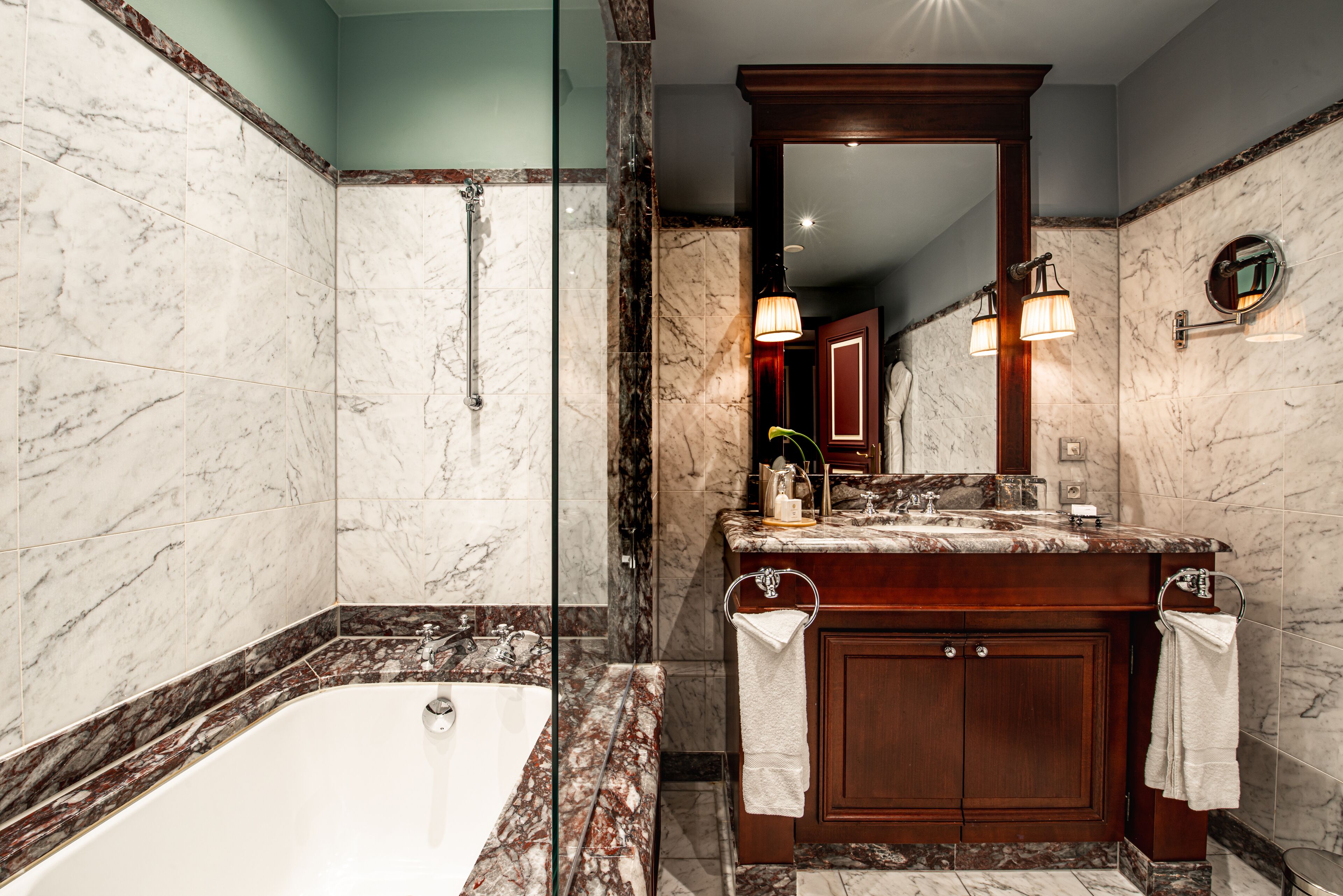 Une salle de bain moderne avec une douche en marbre, une baignoire sur pieds et un meuble-lavabo avec un miroir et un éclairage.
