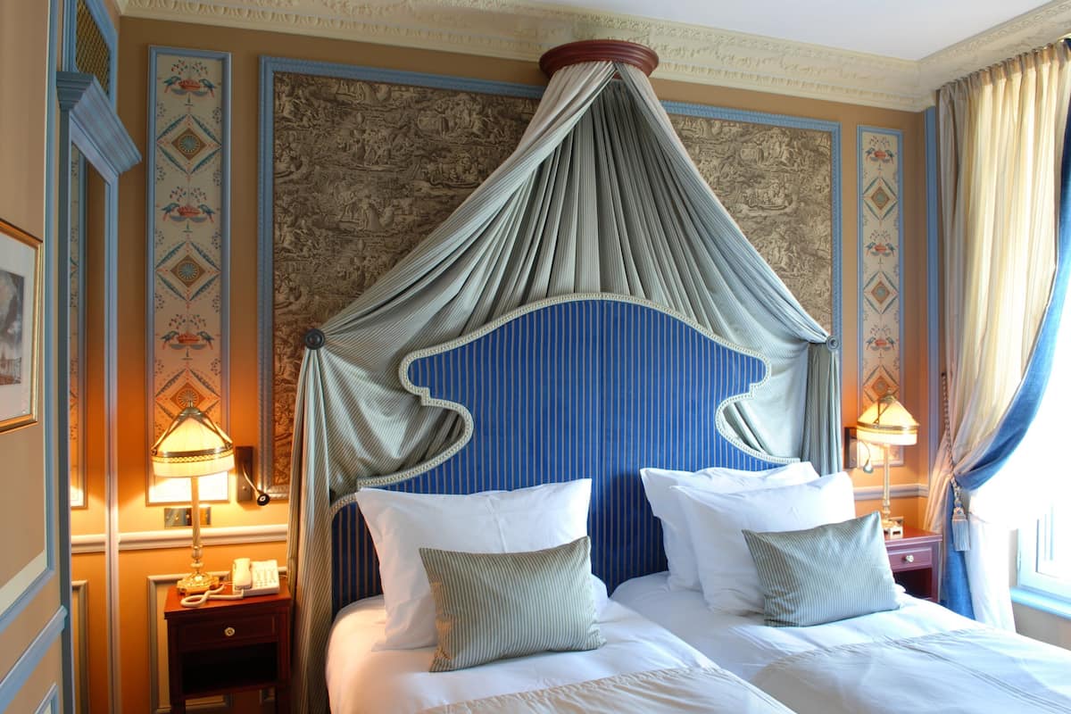 A hotel room with a large bed, two bedside tables with lamps, a canopy bed, and ornate wall decorations.