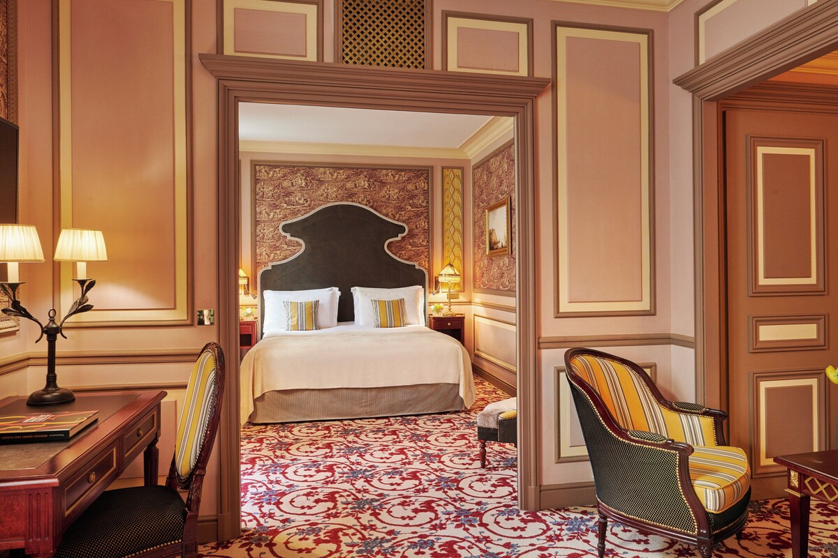 A hotel room with a large bed, a desk with a lamp, a chair, and a decorative wall.
