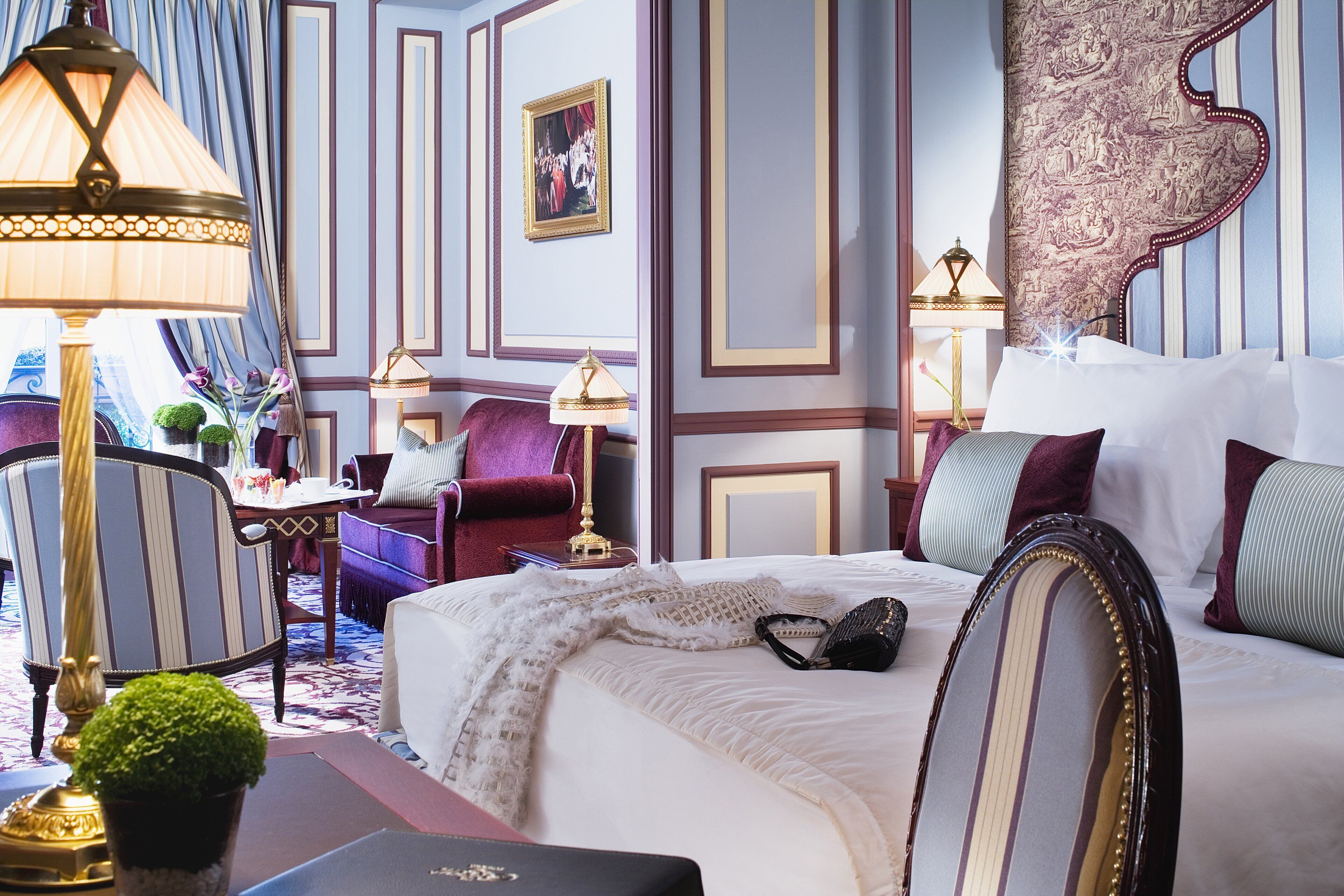A well-appointed hotel room with a large bed, a sitting area with a chair and a small table, and a decorative lamp.
