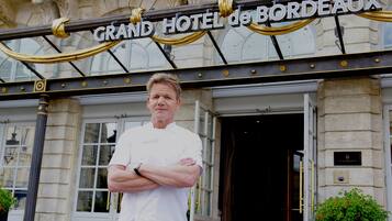 Un hombre está de pie frente al Grand Hotel de Bordeaux, con su nombre visible en letras grandes arriba.