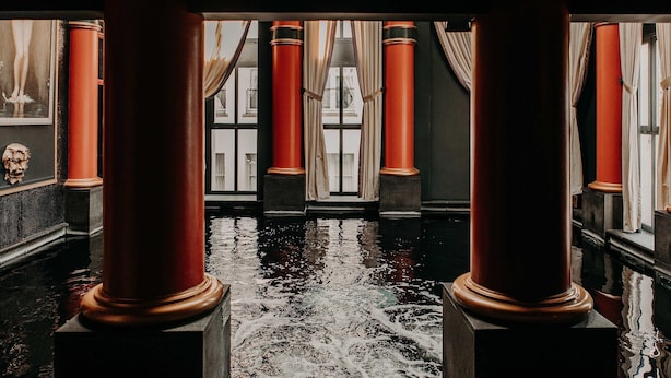 A room with large red columns, a reflective floor, and a view of a building through windows with curtains.