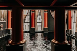 A room with large red columns, a reflective floor, and a view of a building through windows with curtains.