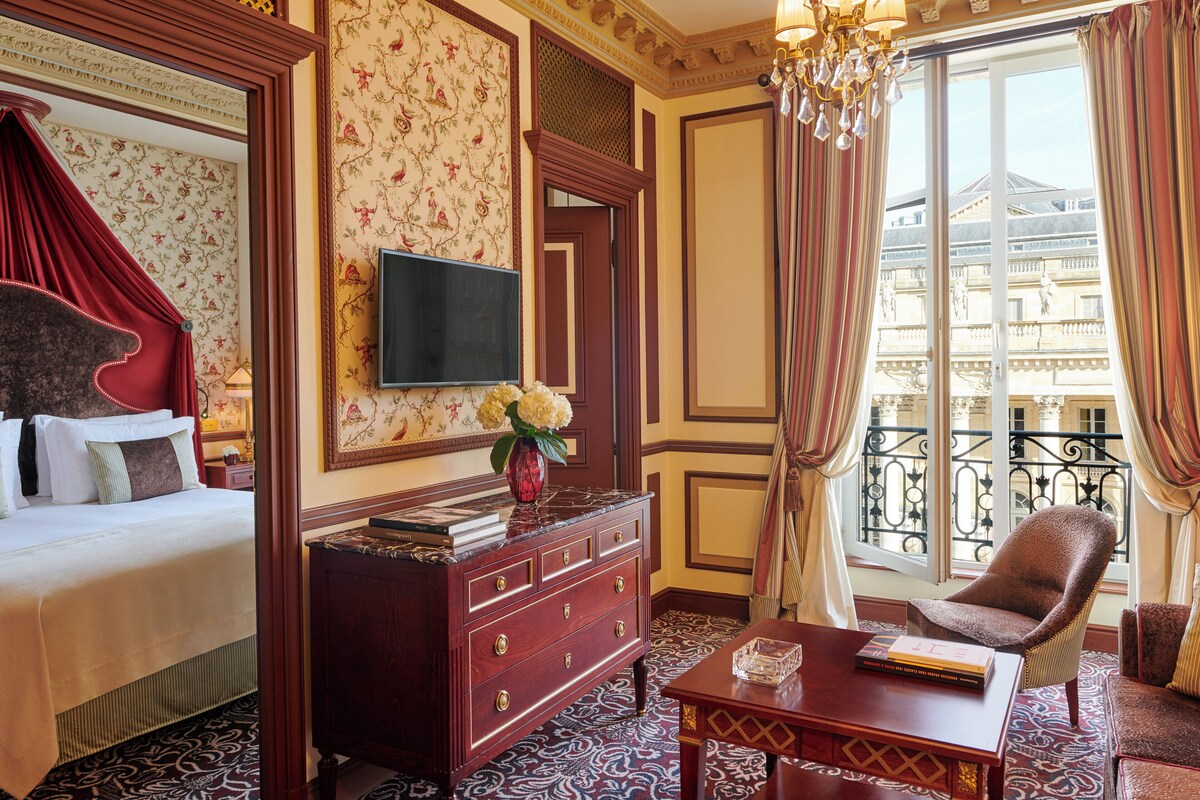 A hotel room with a bed, a dresser, a television, a chair, and a window with a view of a building.