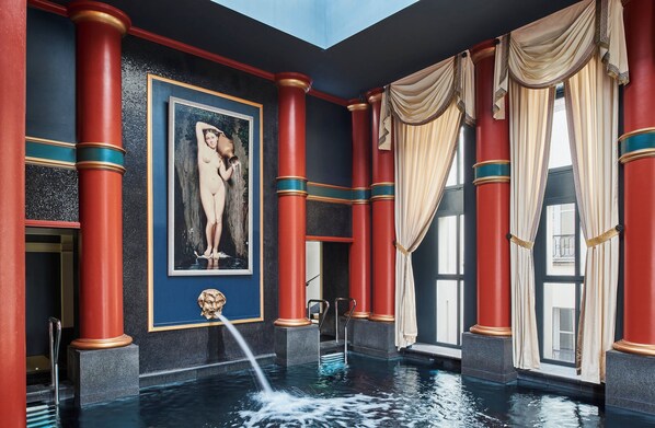 A luxurious indoor pool area with red columns, a framed artwork, and a water feature.