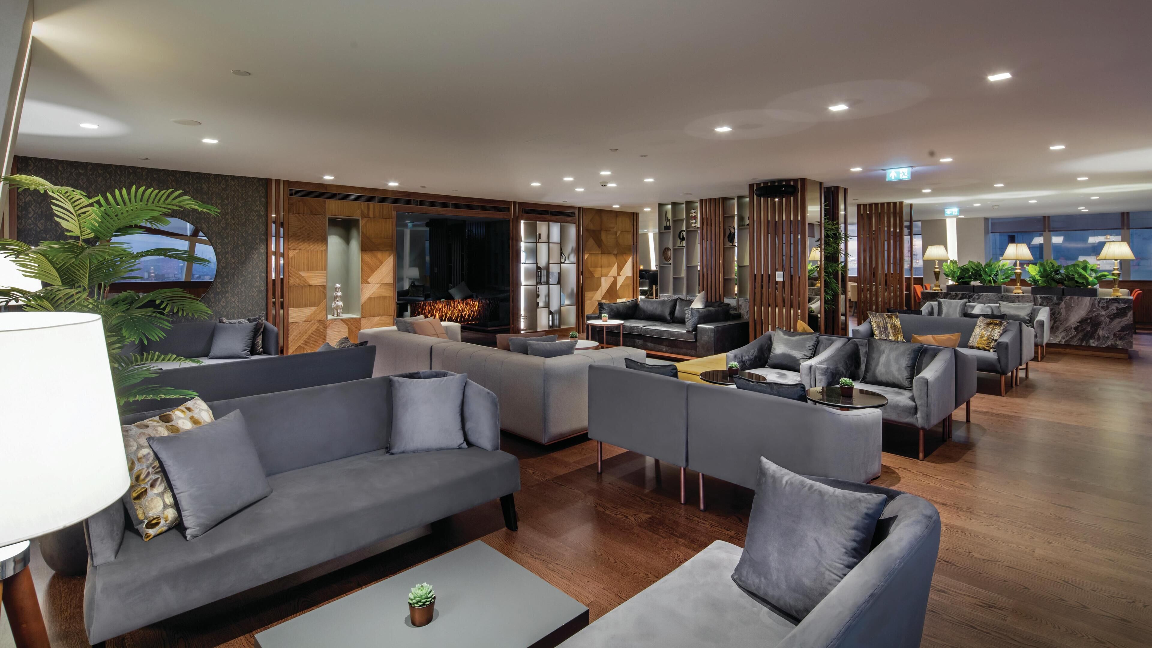 A modern hotel lobby with sofas, armchairs, a fireplace, and a reception desk.