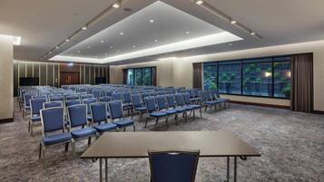 A conference room with rows of chairs, a large table, and a view of greenery through the windows.