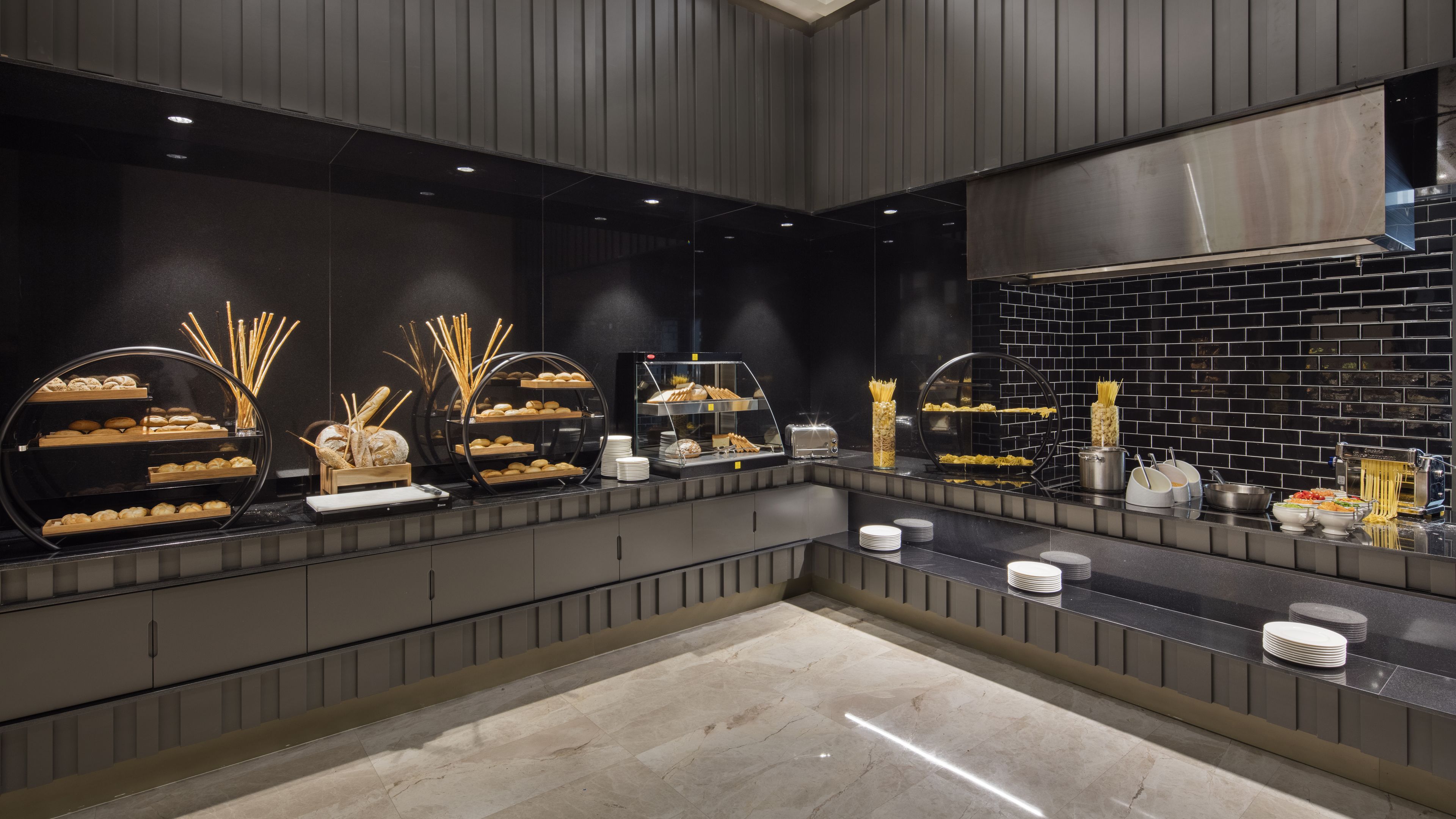 A modern kitchen with a black tiled backsplash, stainless steel appliances, and a variety of baked goods displayed on shelves.