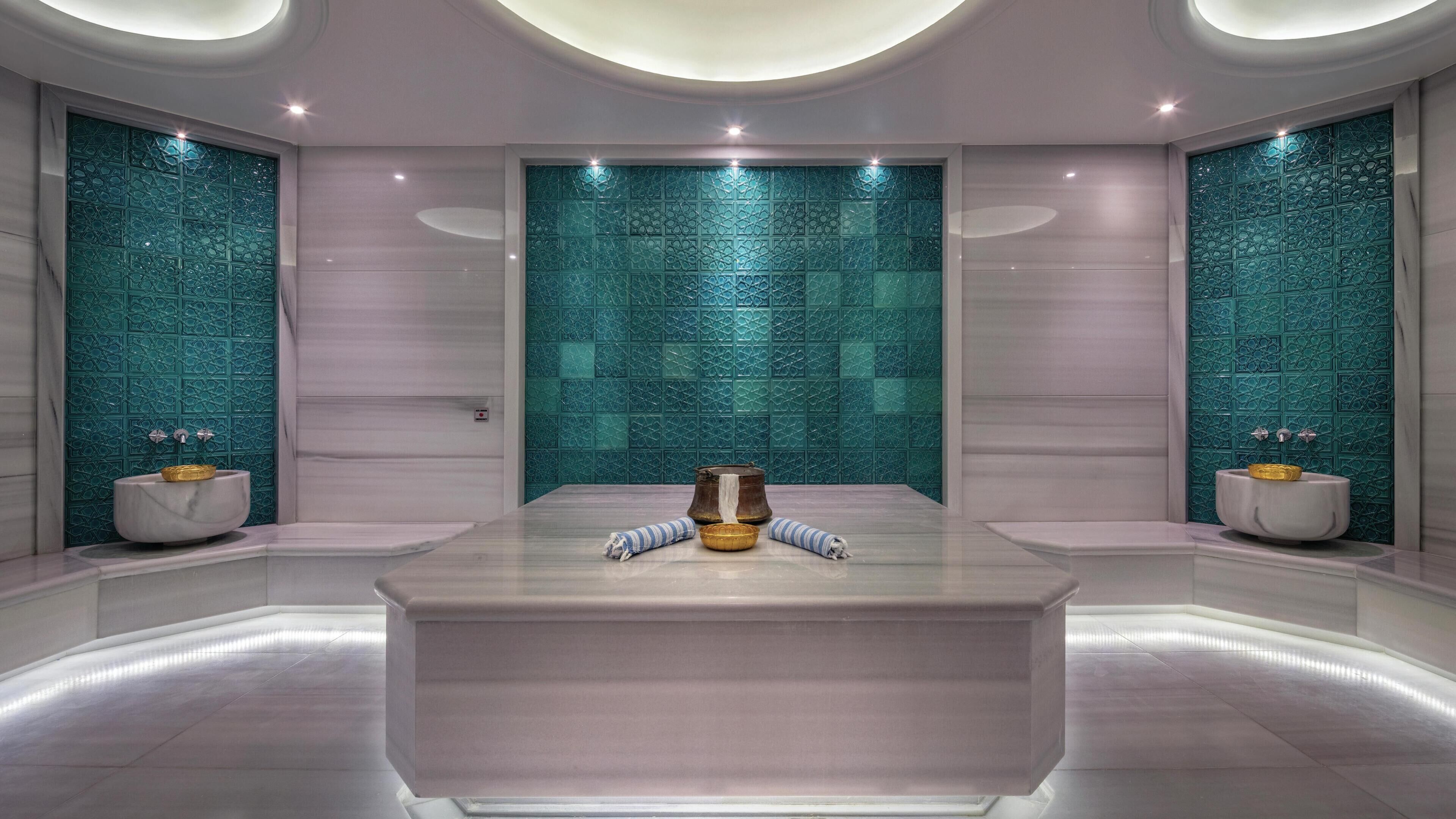 A modern bathroom with a central marble sink, two wall-mounted toilets, and decorative tiles.