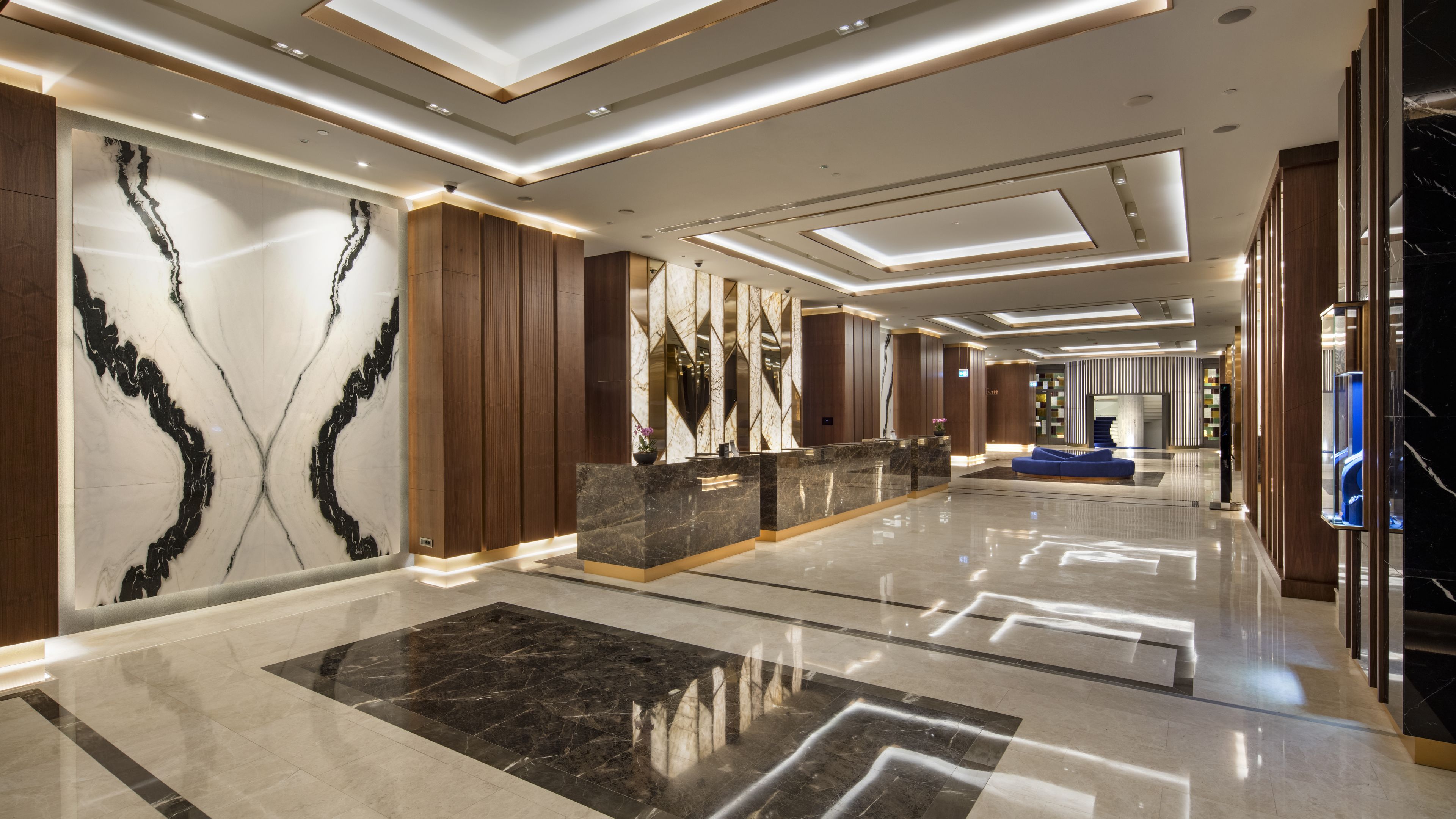 A modern hotel lobby with marble walls, wooden paneling, and a reception desk.