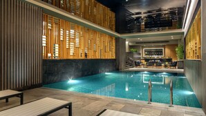 An indoor swimming pool with a modern design, including a wooden partition wall and a seating area with chairs and a table. - Hilton Istanbul Maslak (Sariyer)