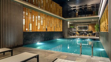 Una piscina interior con diseño moderno, que incluye un separador de pared de madera y una zona de estar con sillas y una mesa.