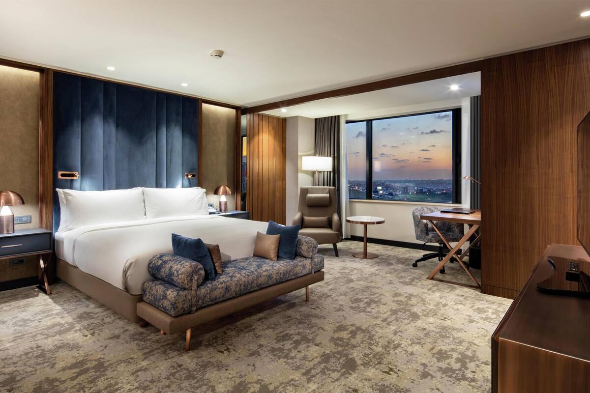 A hotel room with a large bed, a desk, a chair, and a TV.