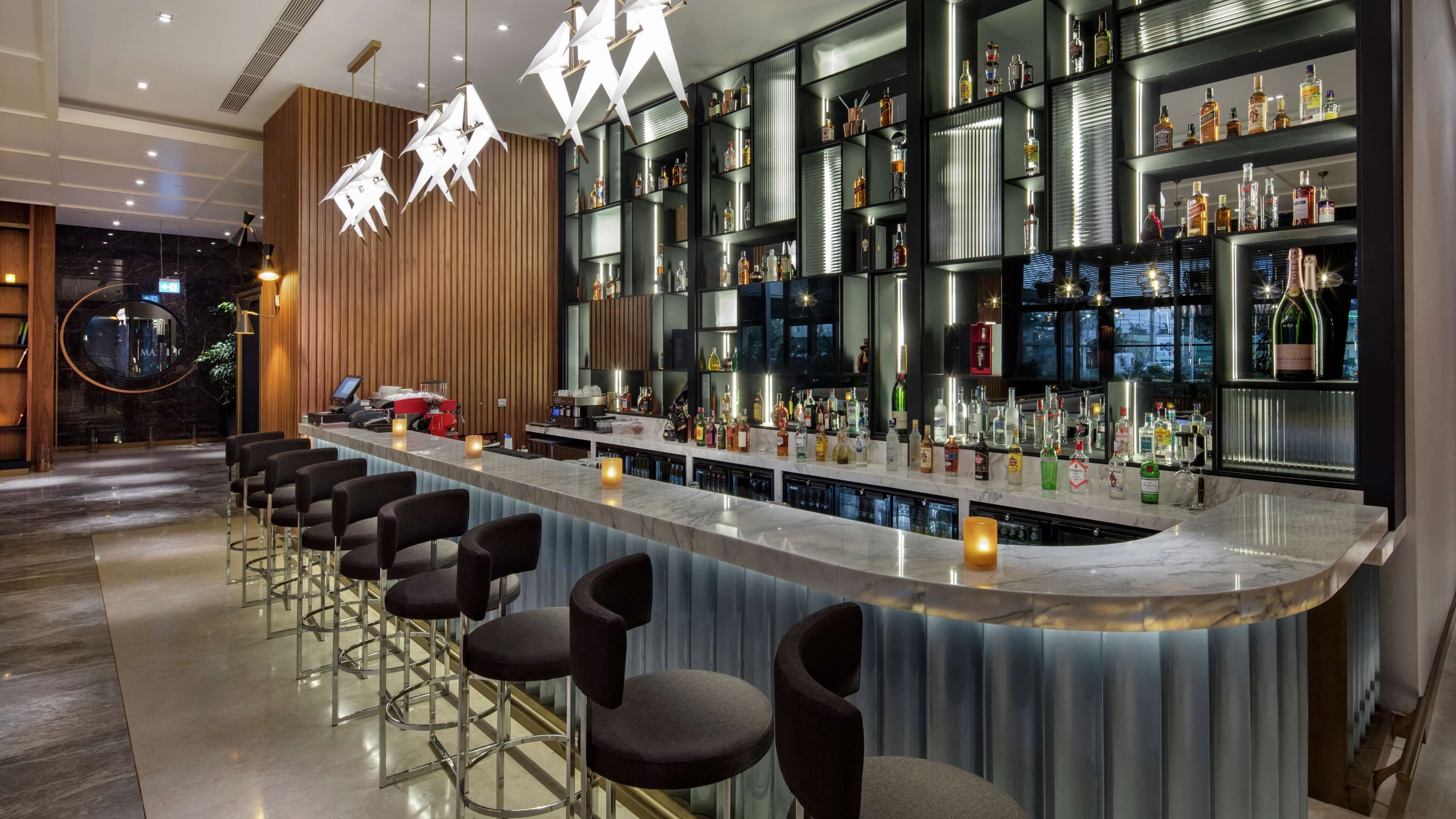Una zona de bar moderna con encimera de mármol, varias botellas de licores y taburetes.