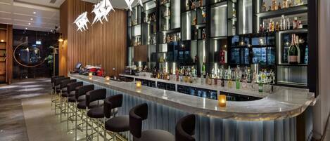 Una zona de bar moderna con encimera de mármol, varias botellas de licores y taburetes.