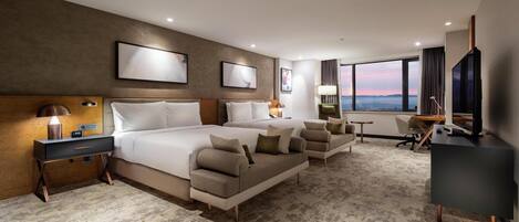 Una habitación de hotel moderna con una cama grande, dos mesitas de noche, un escritorio, una silla y vistas a la ciudad.