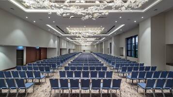 A conference room with rows of blue chairs, a large screen at the front, and a modern chandelier.