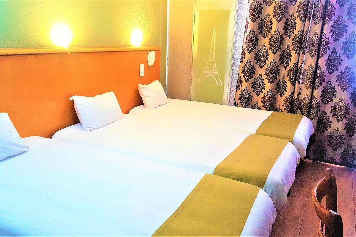 A hotel room with a bed, two pillows, a nightstand, a chair, and a curtain with a floral pattern.