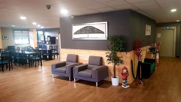 A reception area with two grey sofas, a wooden reception desk, a large framed artwork, and a potted plant. - Euro Hôtel Paris Créteil (Creteil)