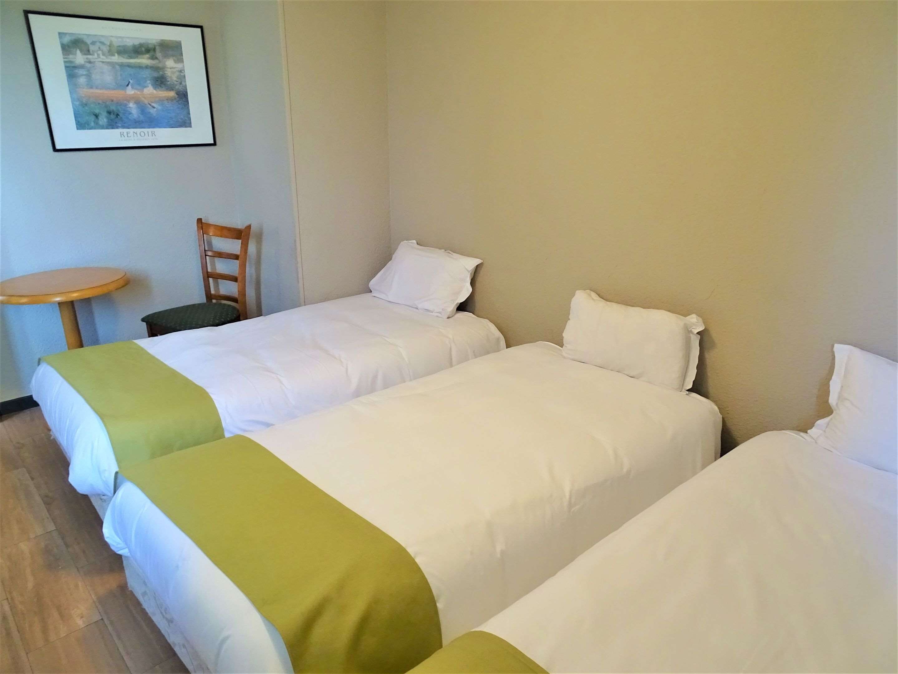 Habitación de hotel con dos camas individuales, una mesita redonda y una silla.