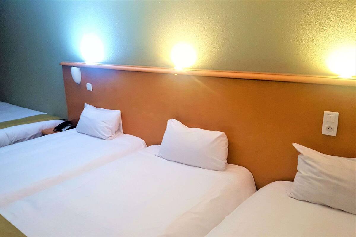 A hotel room with two beds, a wooden headboard, and a wall-mounted light fixture.