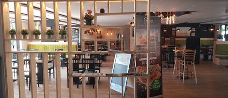 Un restaurante con separadores de madera, asientos acolchados verdes y un cartel con precios de pizza y hamburguesas.