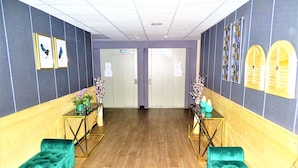 A hotel lobby with a wooden floor, teal sofas, a glass coffee table, and a reception desk with floral arrangements. - Euro Hôtel Paris Créteil (Creteil)