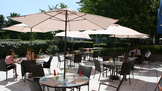 An outdoor patio area with tables and chairs, some under umbrellas. - Euro Hôtel Paris Créteil (Creteil)
