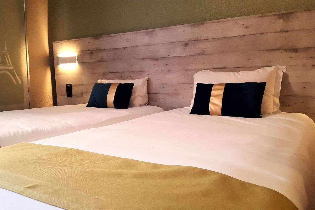 A hotel room with two beds, each with a headboard and pillows. There is a wall-mounted light fixture above the beds.