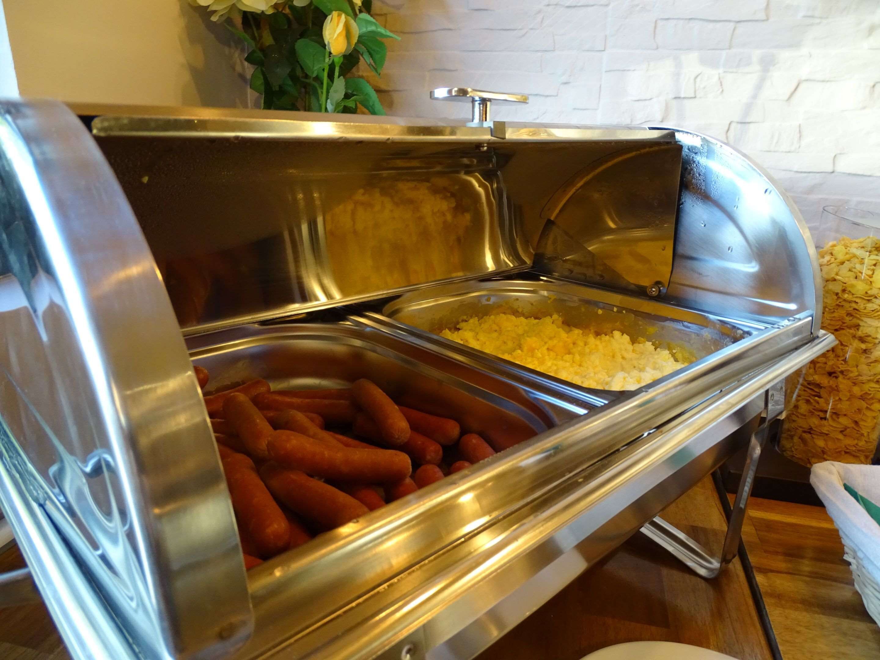 A buffet setup with a variety of food items including hot dogs and a container of rice.