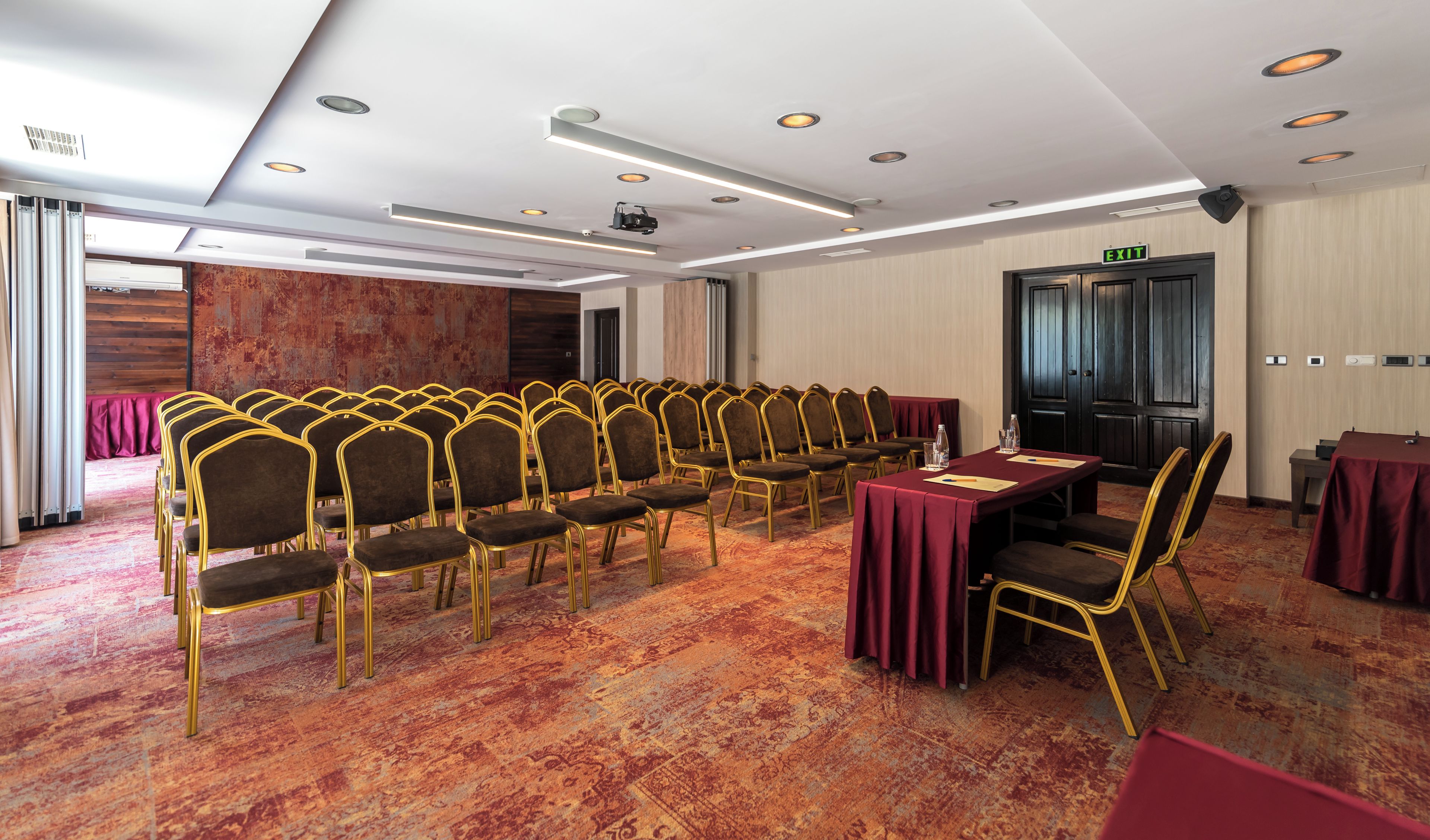 Ein Konferenzraum mit Stuhlreihen, einem Tisch und einem Notausgang.