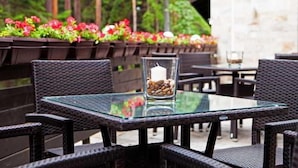 Un espace extérieur aménagé avec des tables à plateaux en verre et des chaises en osier, entouré de jardinières fleuries.